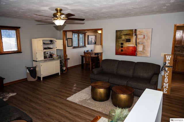 living room featuring ceiling fan, dark wood-type flooring, and a textured ceiling