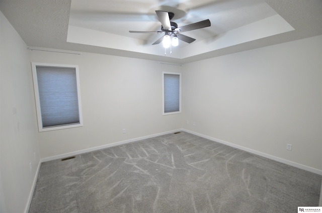 carpeted empty room with ceiling fan and a tray ceiling