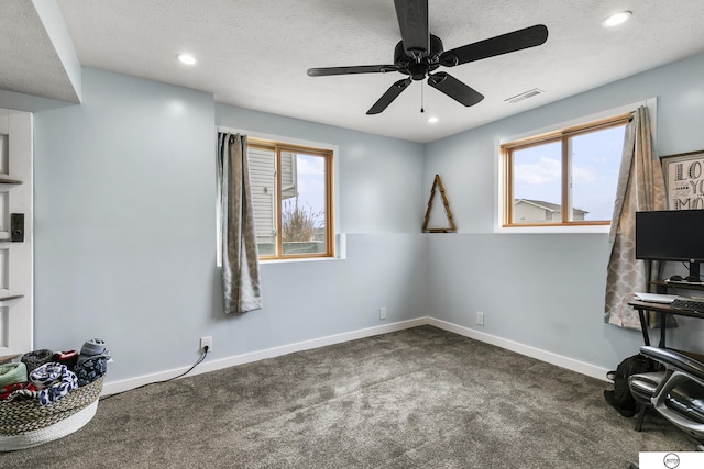 interior space featuring ceiling fan, dark colored carpet, plenty of natural light, and a textured ceiling