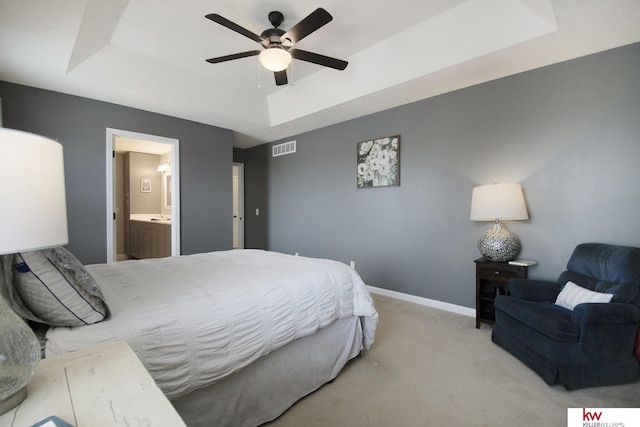 bedroom featuring a tray ceiling, light colored carpet, ceiling fan, and ensuite bathroom