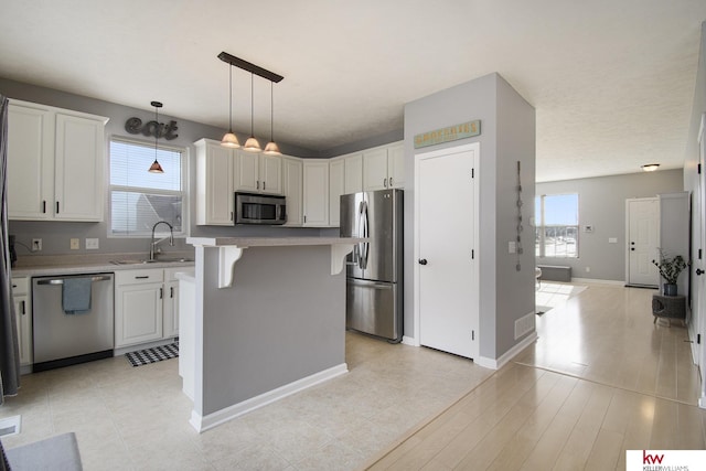 kitchen with white cabinetry, hanging light fixtures, stainless steel appliances, and a kitchen island