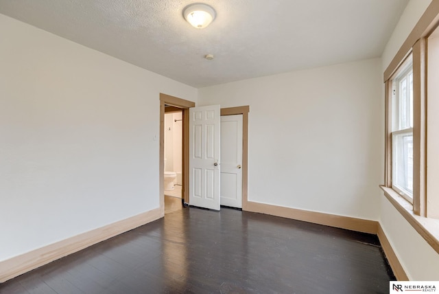 empty room featuring a healthy amount of sunlight, a textured ceiling, and dark wood-type flooring