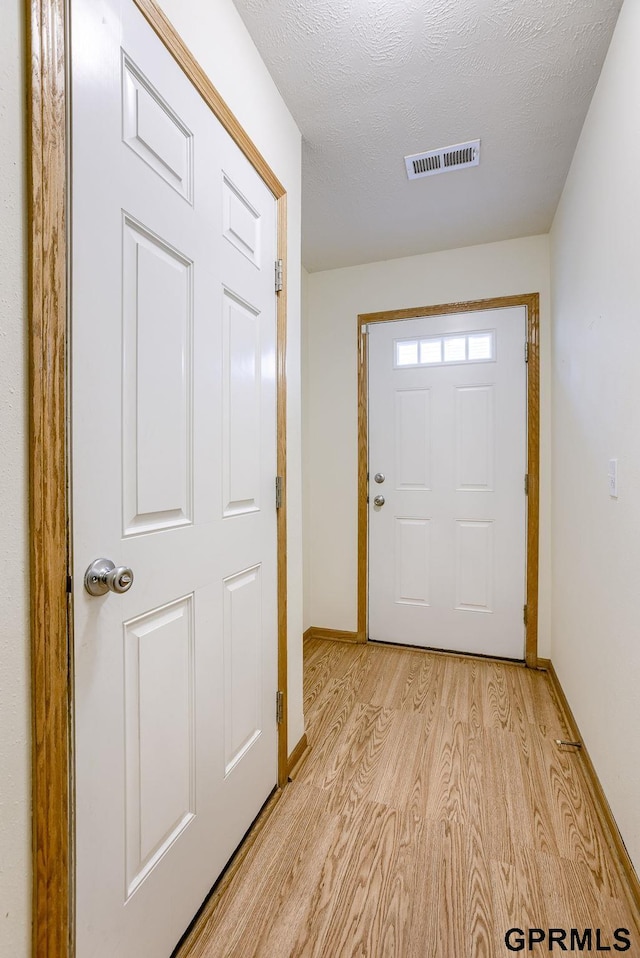 doorway with light hardwood / wood-style floors and a textured ceiling