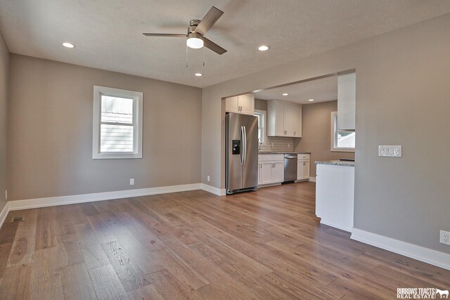 kitchen featuring stainless steel appliances, white cabinetry, a healthy amount of sunlight, and decorative backsplash