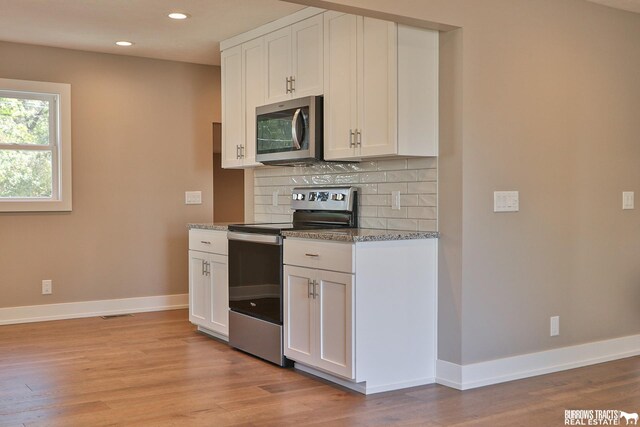 kitchen with appliances with stainless steel finishes, tasteful backsplash, white cabinets, light stone countertops, and light hardwood / wood-style flooring