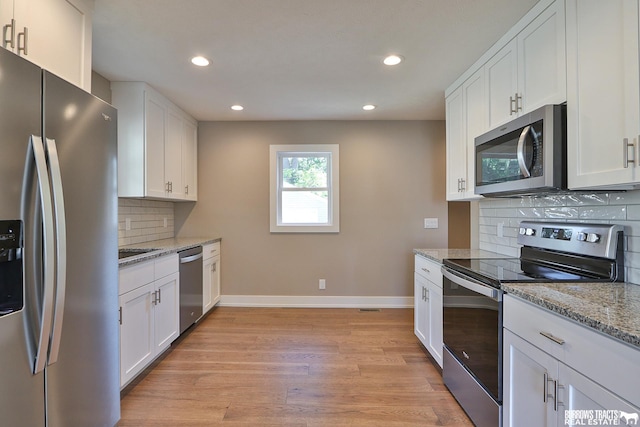 kitchen with light hardwood / wood-style flooring, white cabinets, stainless steel appliances, light stone countertops, and backsplash