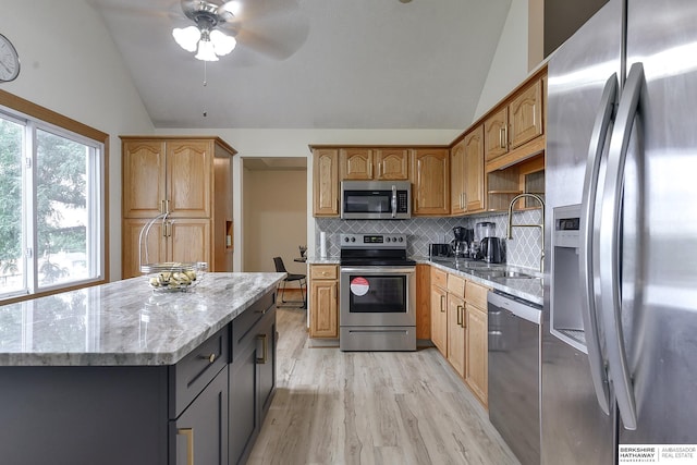 kitchen with appliances with stainless steel finishes, tasteful backsplash, sink, a center island, and light stone counters