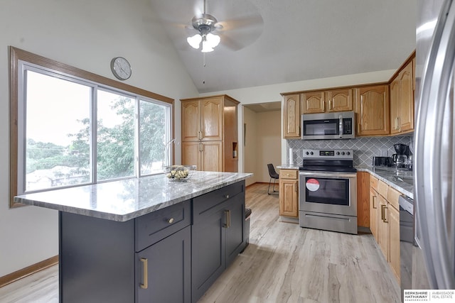 kitchen featuring gray cabinets, appliances with stainless steel finishes, a center island, tasteful backsplash, and light stone countertops