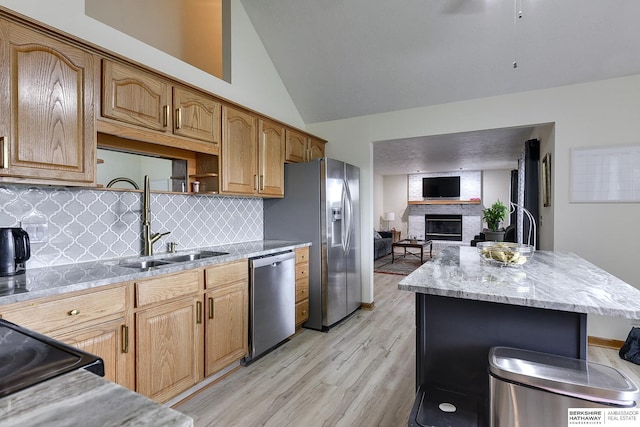 kitchen featuring a fireplace, sink, decorative backsplash, stainless steel appliances, and light wood-type flooring