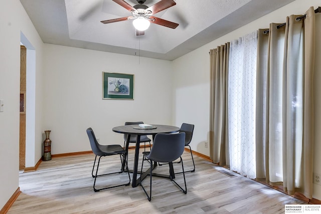 dining area with a raised ceiling, ceiling fan, and light hardwood / wood-style floors