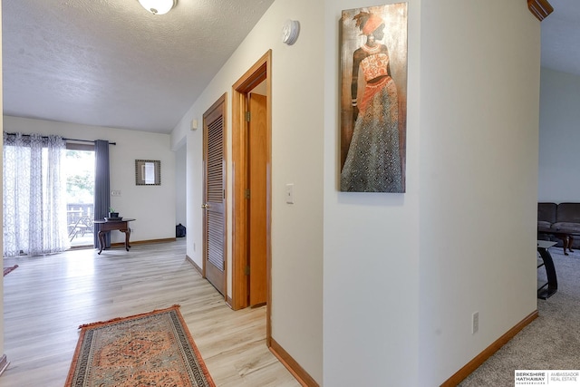 hall with a textured ceiling and light hardwood / wood-style flooring