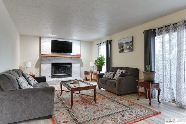 living room with a fireplace, light hardwood / wood-style floors, a textured ceiling, and plenty of natural light