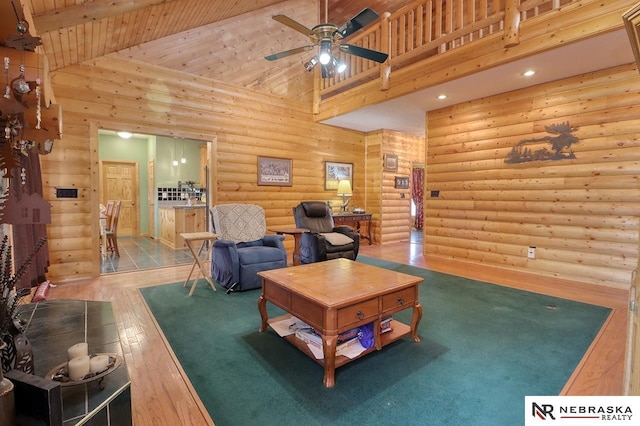 living room featuring hardwood / wood-style floors, high vaulted ceiling, log walls, ceiling fan, and wooden ceiling