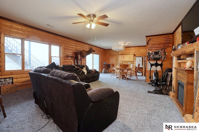 carpeted living room with ceiling fan, a large fireplace, and rustic walls