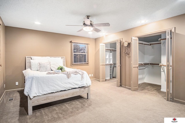 bedroom featuring light colored carpet, two closets, a textured ceiling, and ceiling fan