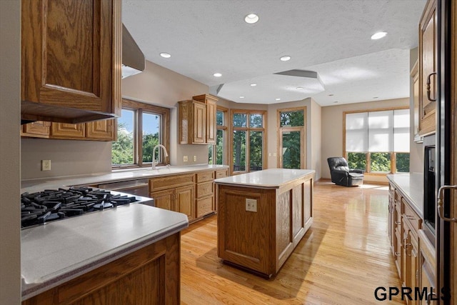 kitchen featuring sink, stovetop, a textured ceiling, a kitchen island, and light wood-type flooring