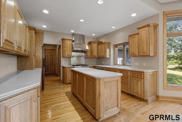 kitchen with appliances with stainless steel finishes, a kitchen island, light hardwood / wood-style flooring, and wall chimney exhaust hood