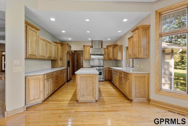 kitchen featuring a kitchen island, appliances with stainless steel finishes, sink, wall chimney range hood, and light hardwood / wood-style flooring