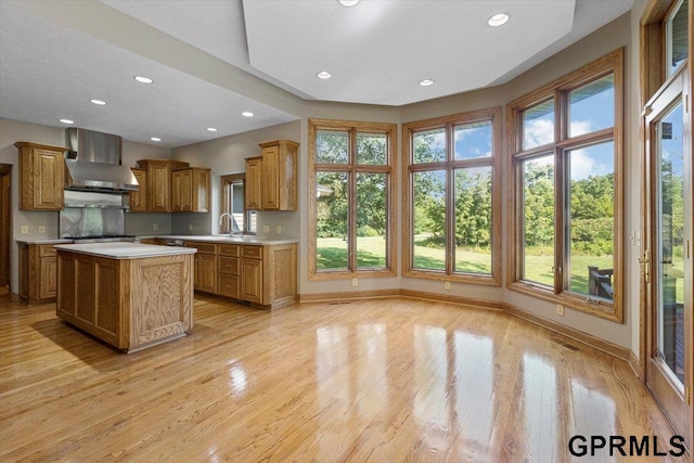 kitchen featuring light hardwood / wood-style flooring, sink, a kitchen island, and wall chimney range hood