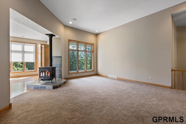 unfurnished living room featuring carpet floors, a healthy amount of sunlight, and a wood stove