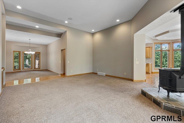 unfurnished living room featuring a notable chandelier, plenty of natural light, light colored carpet, and a wood stove