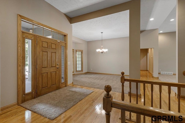 foyer with lofted ceiling, a notable chandelier, light hardwood / wood-style floors, and a textured ceiling