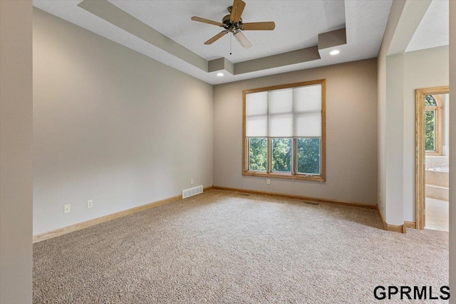 carpeted empty room with ceiling fan, a healthy amount of sunlight, and a raised ceiling