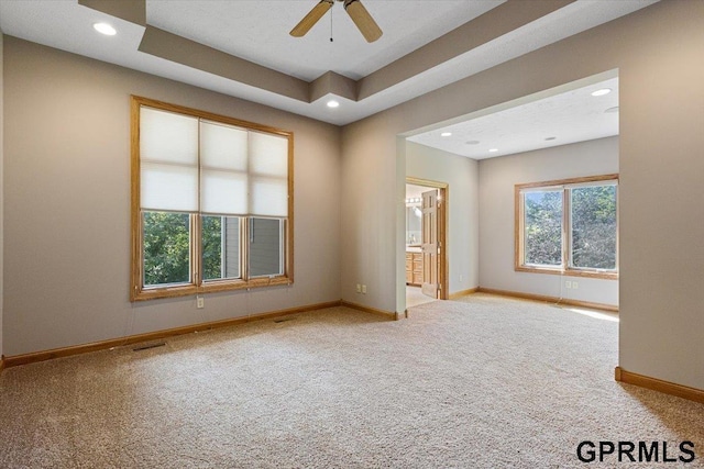 empty room with a raised ceiling, ceiling fan, and carpet flooring