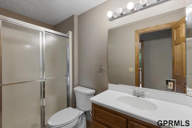 bathroom featuring vanity, toilet, a shower with door, and a textured ceiling