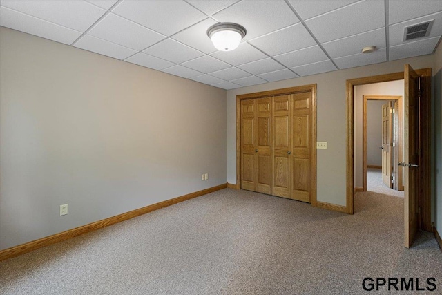 unfurnished bedroom with a drop ceiling, a closet, and carpet