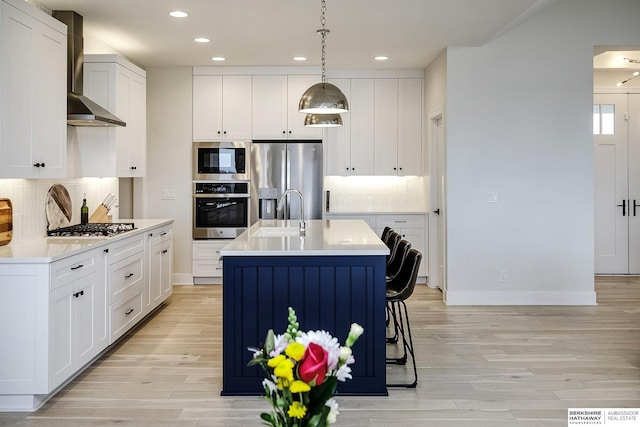 kitchen featuring appliances with stainless steel finishes, pendant lighting, decorative backsplash, a center island with sink, and wall chimney range hood