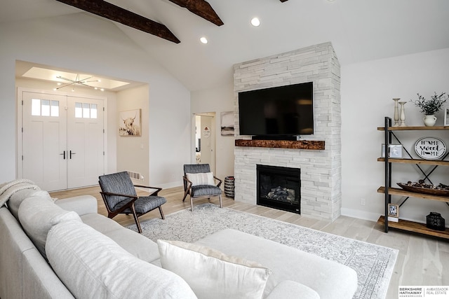 living room featuring vaulted ceiling with beams, light hardwood / wood-style flooring, and a fireplace