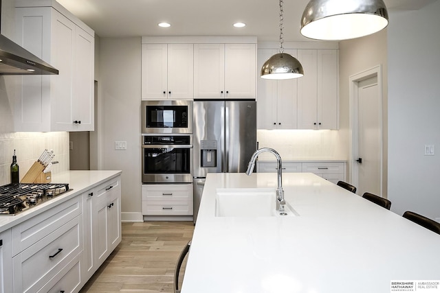 kitchen featuring wall chimney exhaust hood, sink, white cabinetry, appliances with stainless steel finishes, and pendant lighting