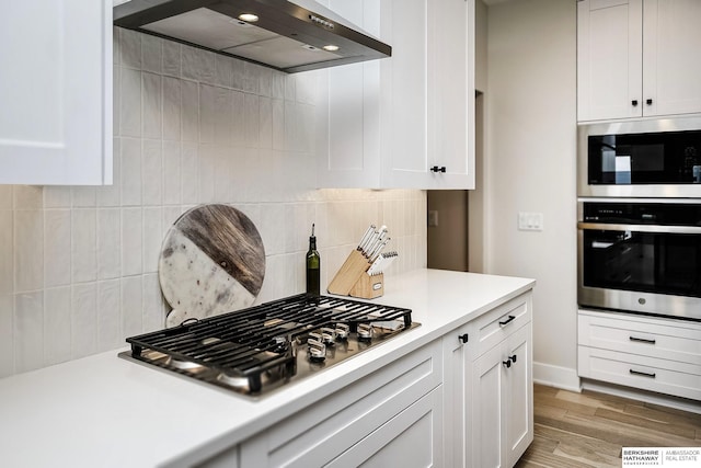 kitchen with stainless steel appliances, white cabinetry, light wood-type flooring, and wall chimney exhaust hood