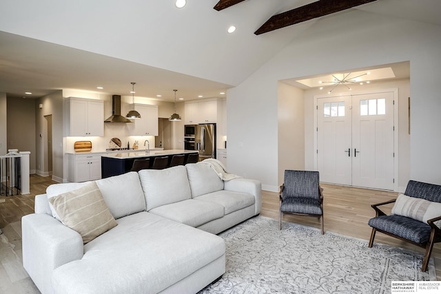 living room featuring vaulted ceiling with beams, an inviting chandelier, and light hardwood / wood-style floors