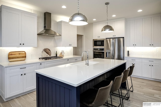 kitchen with stainless steel appliances, sink, a center island with sink, and wall chimney range hood