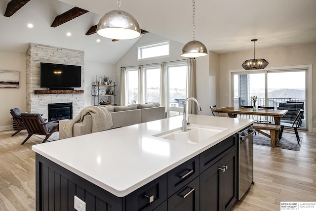 kitchen featuring pendant lighting, a fireplace, dishwasher, sink, and a center island with sink