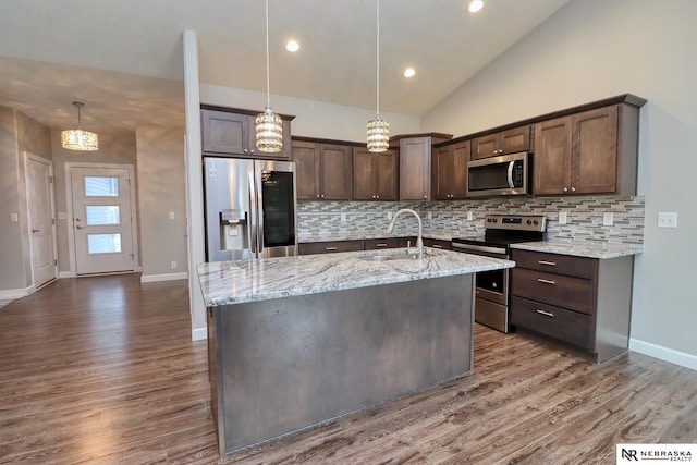 kitchen with dark brown cabinetry, sink, hanging light fixtures, stainless steel appliances, and a kitchen island with sink