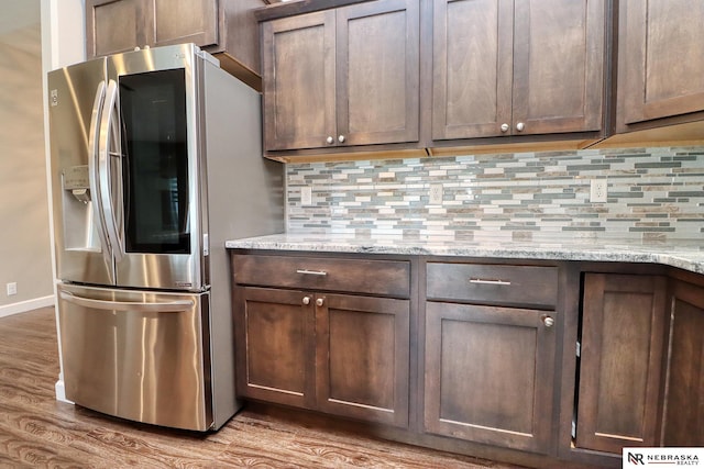 kitchen with light stone counters, dark brown cabinets, stainless steel fridge, and decorative backsplash