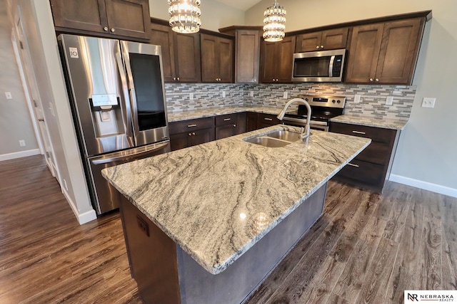 kitchen featuring sink, hanging light fixtures, an island with sink, stainless steel appliances, and light stone countertops