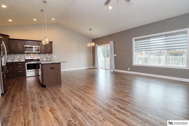 kitchen with pendant lighting, dark brown cabinets, stainless steel appliances, a kitchen island, and decorative backsplash