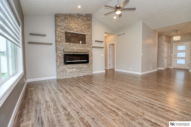 unfurnished living room with lofted ceiling, a stone fireplace, wood-type flooring, and ceiling fan