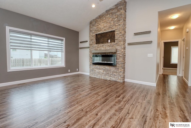 unfurnished living room with lofted ceiling, a stone fireplace, and wood-type flooring