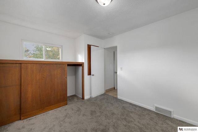 unfurnished bedroom with light colored carpet, a textured ceiling, and a closet