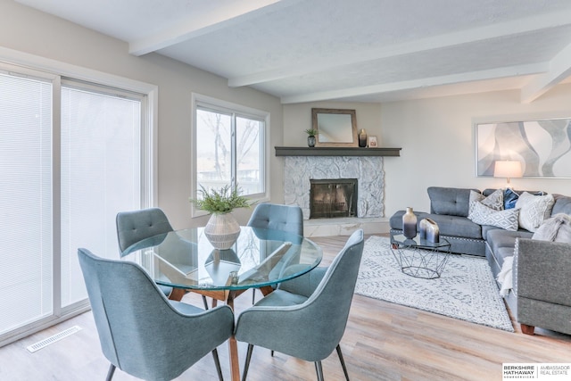 dining room with beamed ceiling, a stone fireplace, and hardwood / wood-style flooring