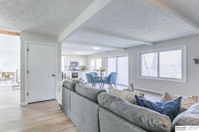 living room featuring beamed ceiling, sink, a textured ceiling, and light hardwood / wood-style floors