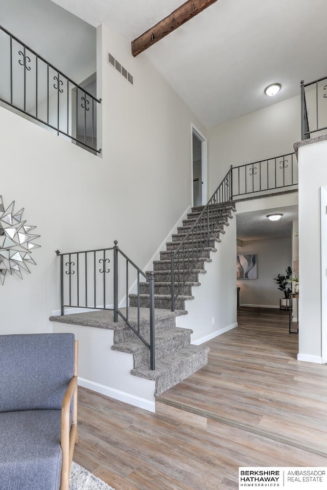 stairs featuring hardwood / wood-style flooring, a high ceiling, and beam ceiling