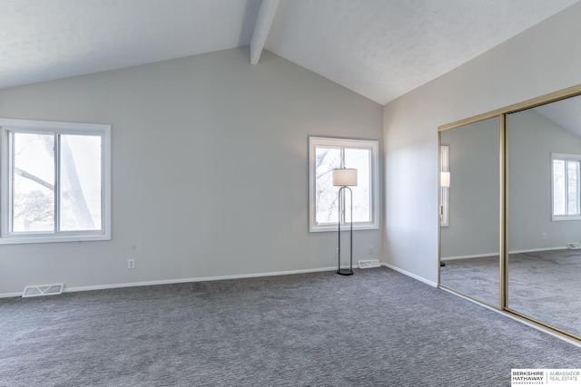 unfurnished bedroom with multiple windows, lofted ceiling with beams, a closet, and dark colored carpet