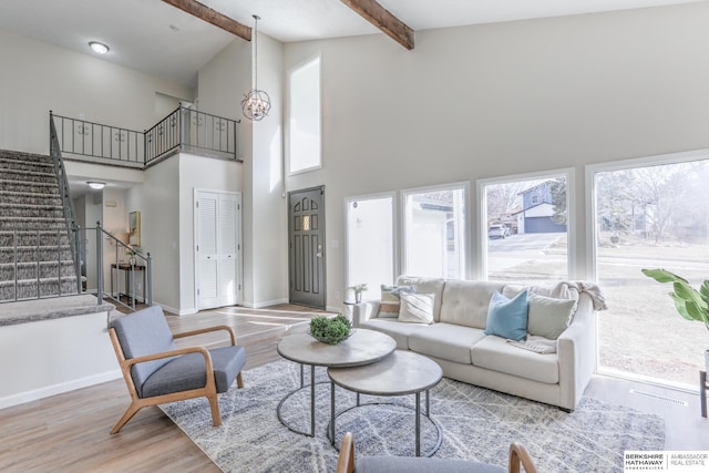 living room with a notable chandelier, beam ceiling, light hardwood / wood-style flooring, and a towering ceiling