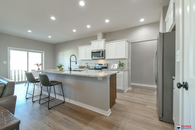 kitchen featuring sink, a kitchen island with sink, stainless steel appliances, light hardwood / wood-style floors, and white cabinets